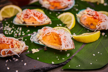 Mussels with vermicelli, lying on a leaf of a green plant in a restaurant. Funchosa vermicelli (glass noodles) with seafood and lemon, salt and spices scattered on the table