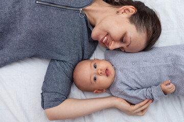 Young mother with 5 month old baby lie on the bed, top view