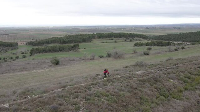 Filmaci&oacute;n a&eacute;rea con dron siguiendo a un hombre joven montado en bicicleta de monta&ntilde;a descendiendo por un sendero.