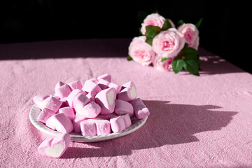 Pink heart shape, strawberry flavored Marshmallows on white plate on table with pink tablecloth. Roses in background. Love theme, Valentine concept.