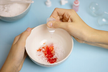 a child makes a bath bomb from sea salt, citric acid, soda, dye and flavor on a blue background, instructions, step 2