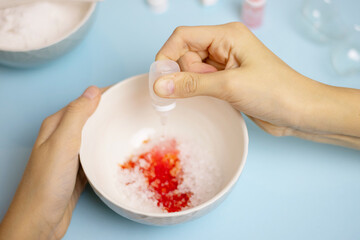 a child makes a bath bomb from sea salt, citric acid, soda, dye and flavor on a blue background,...