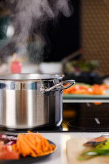 Cooking in the kitchen. Sliced vegetables on a plate. Boiling water in a saucepan on an induction stove.