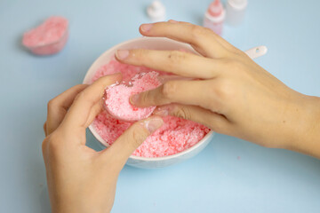 a child makes a bath bomb from sea salt, citric acid, soda, dye and flavor on a blue background,...