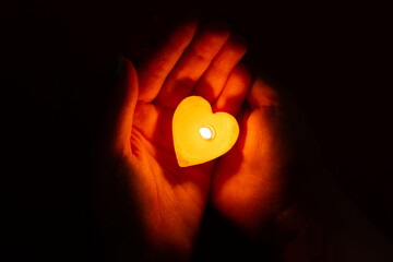 Woman hands holding a candle in the form of a heart on a black background. Charity and giving back....