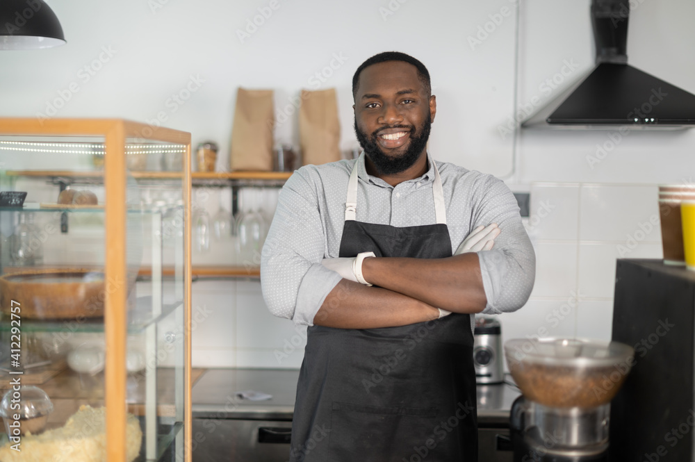 Wall mural Cheerful and friendly African-American small business owner, cafe manager, bakery staff stands in confident pose with arms crossed and looks at the camera