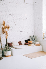 Interior design of bright living room with white walls and couch bench with pillows. Dried high plants near wall.