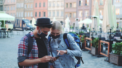 Young tourists in protective masks and with bags using smartphone. They looking for interesting tourist attractions.