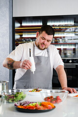 The male chef adds olive oil from a white bottle to the salad sauce.