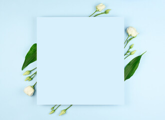 Spring composition. White flowers, paper blank on pastel blue background. Flat lay, top view, copy space, mock up.