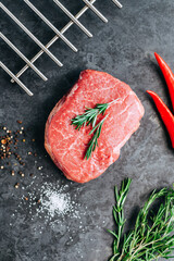 Raw beef steak on black background with rosemary, chili pepper and spices.