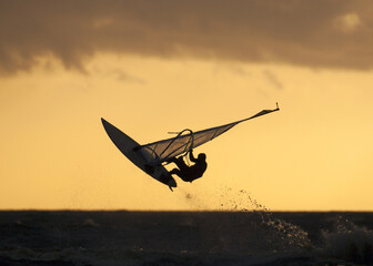 Cool shot of  the silhouette of a windsurfer in the air at golden hour - Powered by Adobe