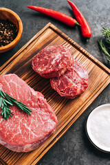 Raw beef steak and minced round steak for burgers on wooden board with rosemary, chili pepper and spices .