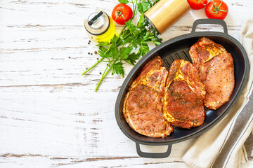 Fresh raw pork loin on the bone with spices and marinade in a cast iron pan on wooden table, preparation for baking. Top view flat lay. Copy space.