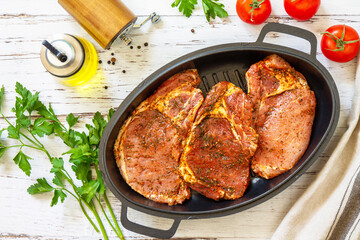 Fresh raw pork loin on the bone with spices and marinade in a cast iron pan on wooden table, preparation for baking. Top view flat lay.