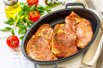 Fresh raw pork loin on the bone with spices and marinade in a cast iron pan on wooden table, preparation for baking.