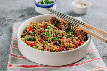 Fried Rice with vegetables, green onion and sesame in white bowl on stone background.