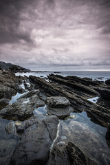 Fototapeta na wymiar atardecer en la costa sobre el mar, con rocas en primer plano y muchas nubes