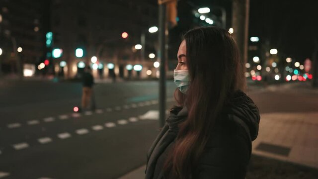 Female model wearing mask against virus, walking alone in the night city and crossing street. Background lights of transportation. Coronavirus covid-19 pandemic concept