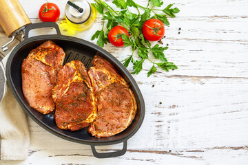 Fresh raw pork loin on the bone with spices and marinade in a cast iron pan on wooden table, preparation for baking. Top view flat lay. Copy space.