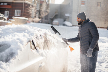 A young man cleans his car after a snowfall on a sunny, frosty day.