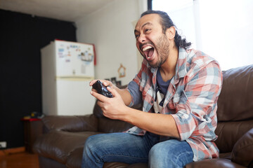 hispanic man sitting on the sofa at home, playing a video game