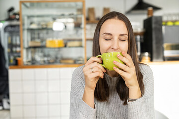 Smiling woman with eyes closed enjoys a morning coffee sitting in the cozy cafe, a calm female with cup of hot drinks indoor