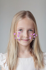 Close-up portrait of smiling little caucasian girl with taped gypsophila on face isolated on grey background. Model in studio. Trendy creative idea