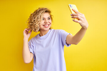 female posing making photo on smartphone, selfie, smiling. indoor studio shot isolated on yellow background