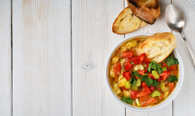Minestrone soup in white dish on white wooden table, top view. Italian soup with seasonal vegetables. The concept of delicious healthy vegetarian food. Diet idea nutrition. Flat lay with copy space