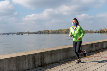 Young active sporty fitness jogger woman or girl jogging and running outdoor with protective medical mask on her face to keep healthy life routine protected from coronavirus or COVID-19 virus  