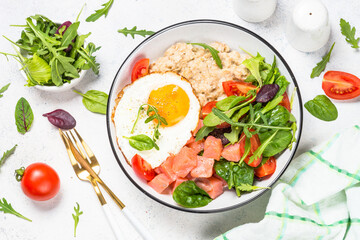 Savory breakfast. Oatmeal porrige with salted salmon, egg and fresh salad. Healthy food, balanced nutrition. Top view on white table.
