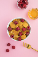 Top view of mini pancakes with raspberries in the white bowl on the pink surface