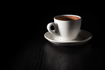 Cup of coffee on black wood table. White porcelain cup on saucer. Copy space.