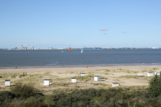 the coast in breskens, zeeland, the netherlands with beach houses in the dunes behind the sand beach and surfers in the westerschelde sea in summer