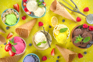 Various colorful ice cream balls in different bowls, with ice cream waffles cones and flavor ingredients - pistachio nuts, berries, lemon, chocolate, vanilla, mint. Trendy yellow bright background