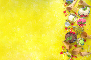 Various colorful ice cream balls in different bowls, with ice cream waffles cones and flavor ingredients - pistachio nuts, berries, lemon, chocolate, vanilla, mint. Trendy yellow bright background