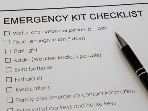 An emergency kit checklist printed on white paper and ink pen are shown close.