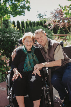Smiling, caucasian senior couple outside with wheelchair in garden