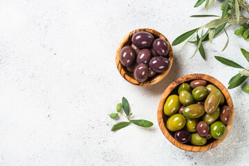 Olives in wooden bowl on white stone background. Top view with copy space.
