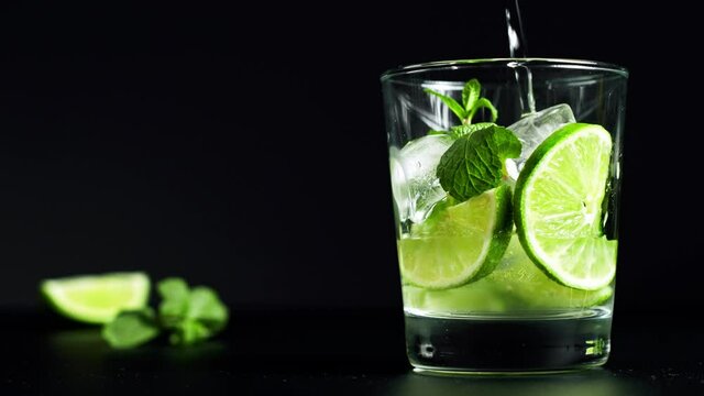 Close-up refreshing soda tonic. Pour carbonated water into a glass of lime and ice. Cold Mojito lemonade. Packshot. 4K UHD