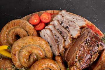 A large meat plate. Smoked pork sausages, grilled chicken, beef, pork, on a large plate on a dark background