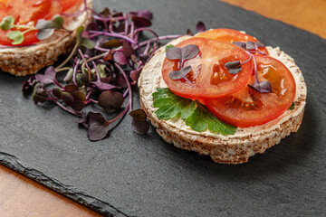 dietetic crispbreads with curd cheese, tomatoes and radish sprouts on a slate board