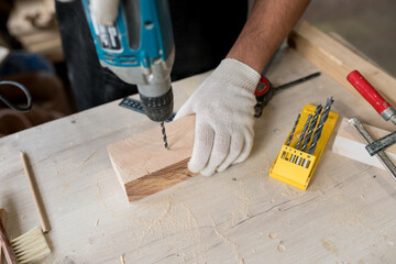 Close-up of carpenter using electric drill in workshop. Man drilling wood on table. Joinery work on...