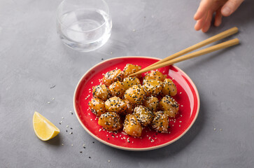 Traditional сhinese fried apples in caramel with sesame seeds on red vintage plate with chopsticks on gray background
