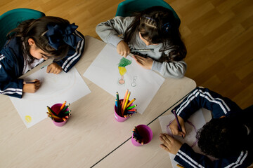 tres niños dibujando en una mesa en el colegio visto desde arriba