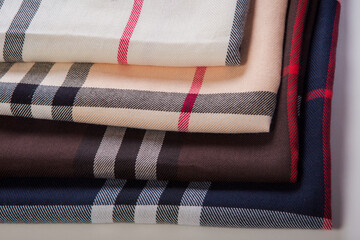 closeup at set of folded milky, beige, brown and black checked scarf with strips