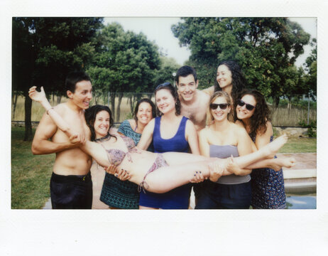 Polaroid shot of friends holding brunette in bikini near pool