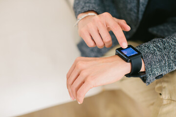 Detail of a woman touching her digital smartwatch at office.
