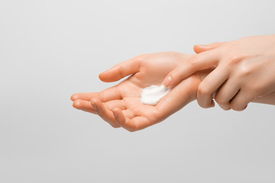 A girl smearing a handful of hand cream on her hand. Photo on gray background.